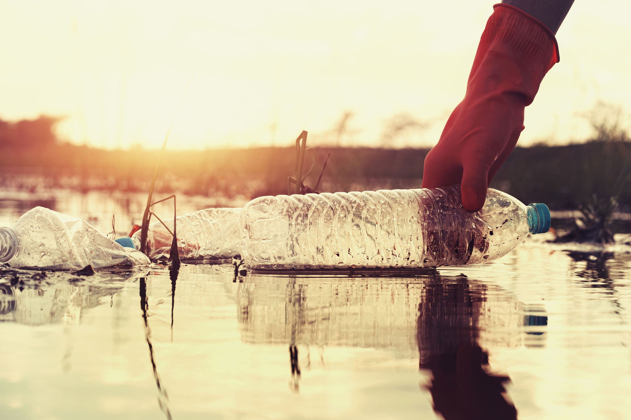 woman hand picking up garbage plastic for cleaning at river with sunset