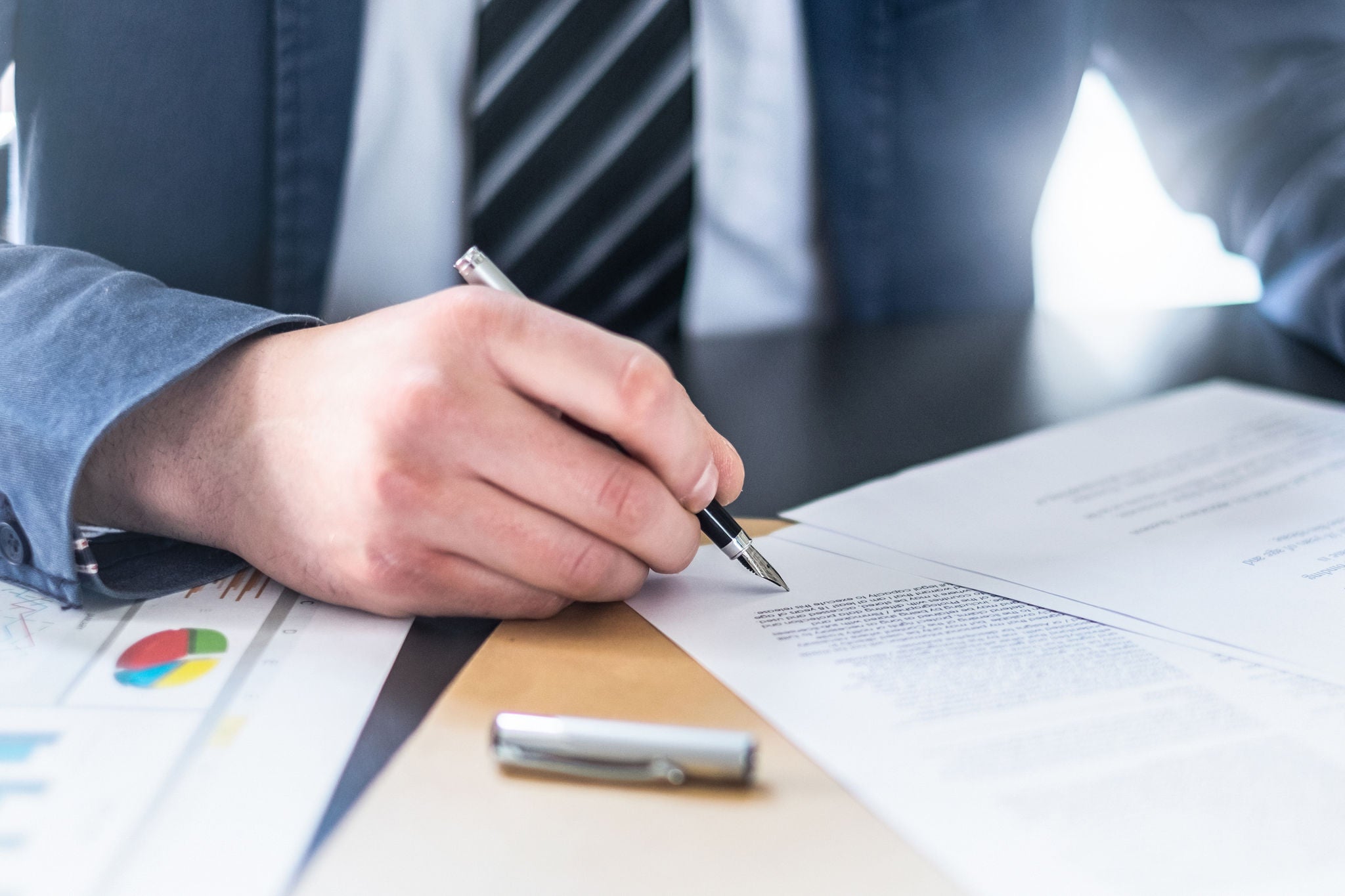 Business man signing contract document on office desk, making a deal.