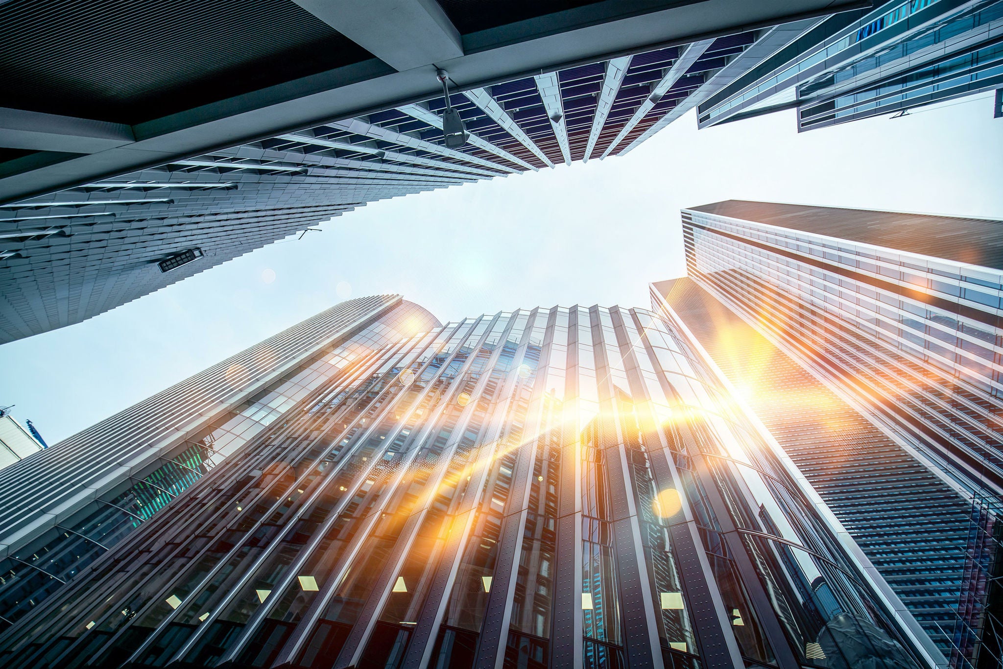 An upward view of modern office buildings in a UK city, with sunlight shining through the glass windows.