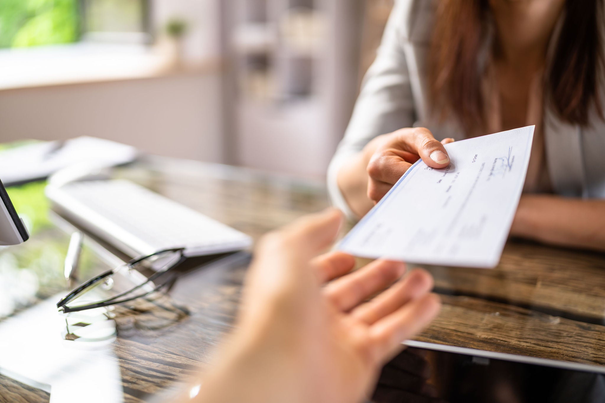Close-up Of A Businesswoman Giving Cheque To Her Colleague At Workplace In Office