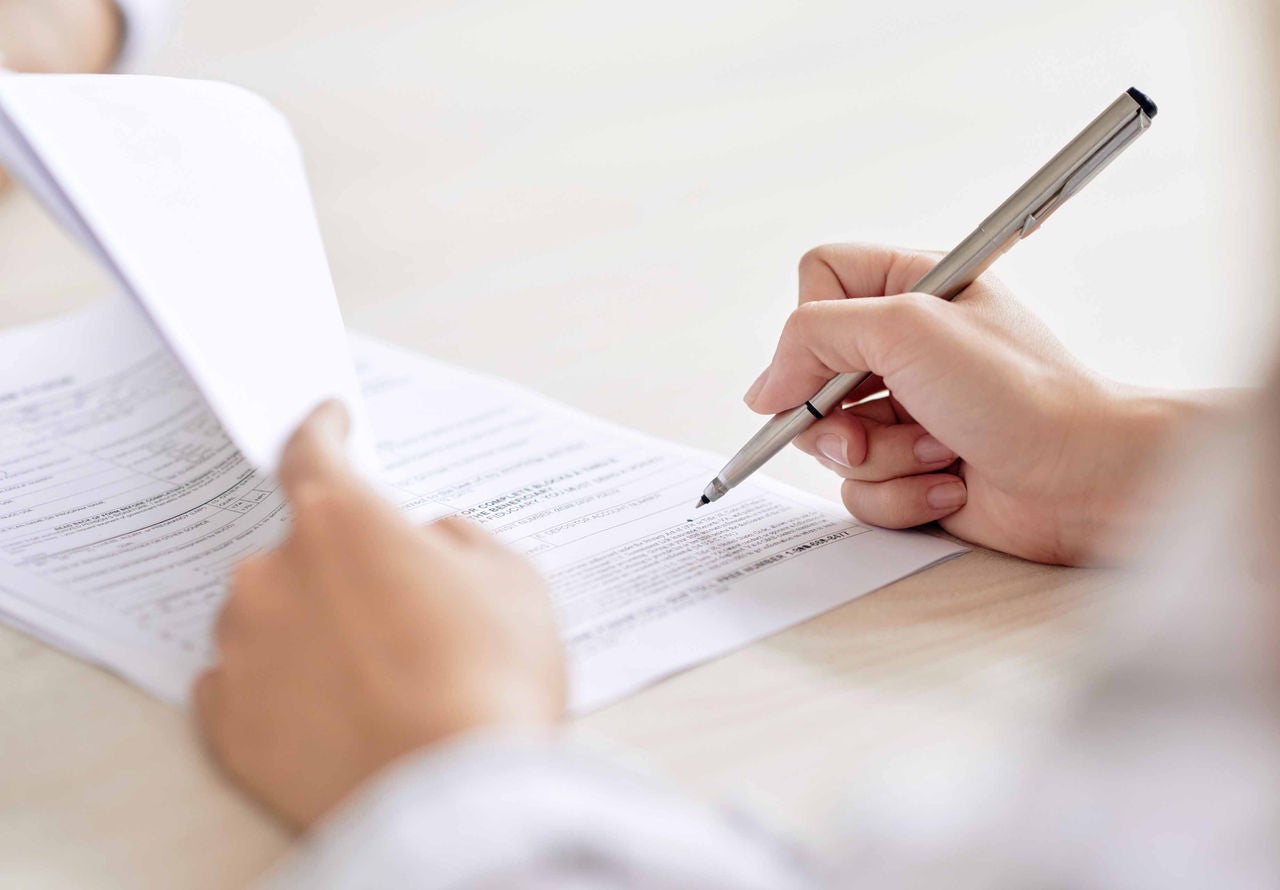 Crop shot of person with pen signing contract at desk in daylight