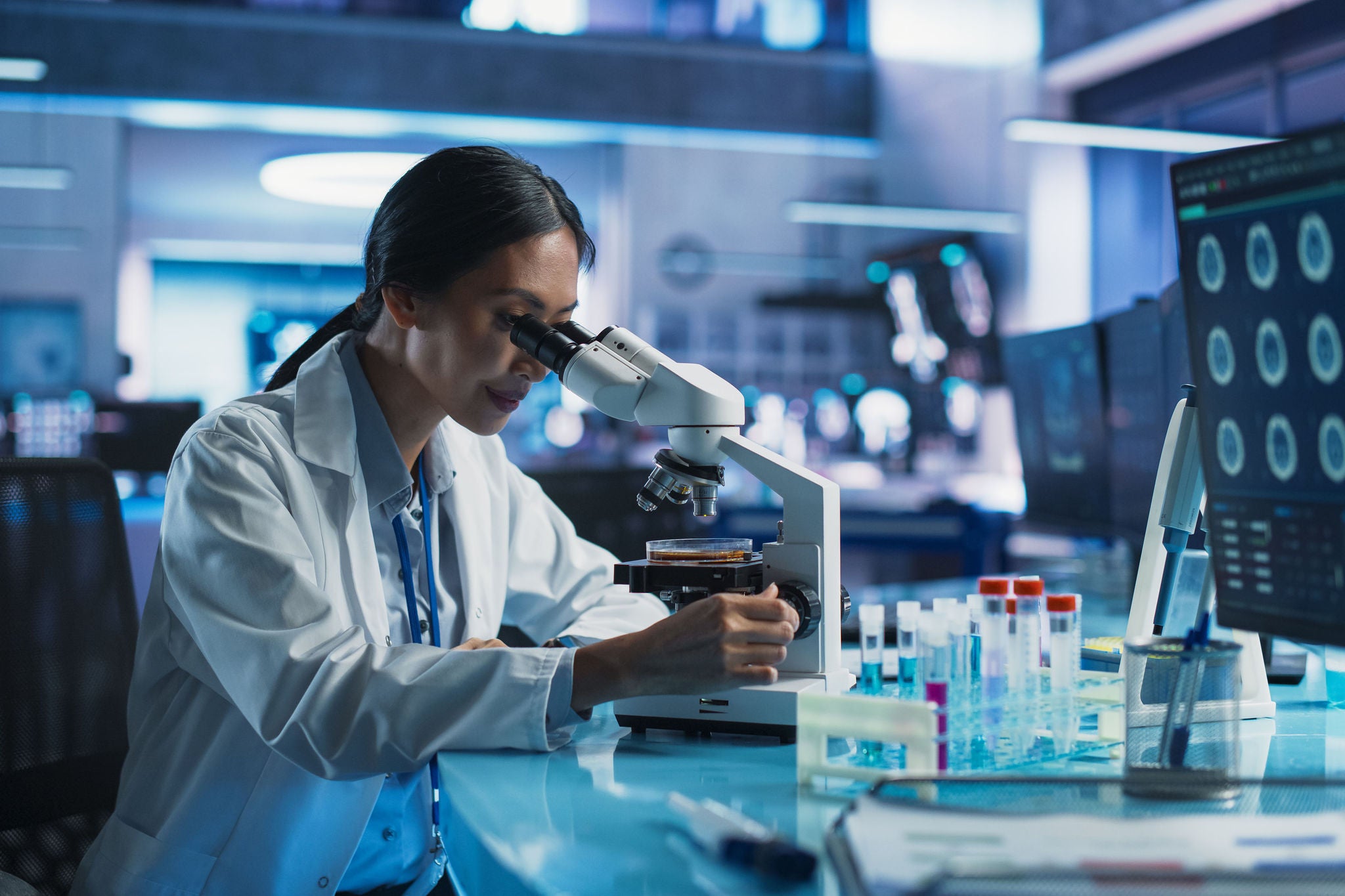 Medicine Development Laboratory: Asian Female Scientist Using Microscope, Analyzes Petri Dish Sample