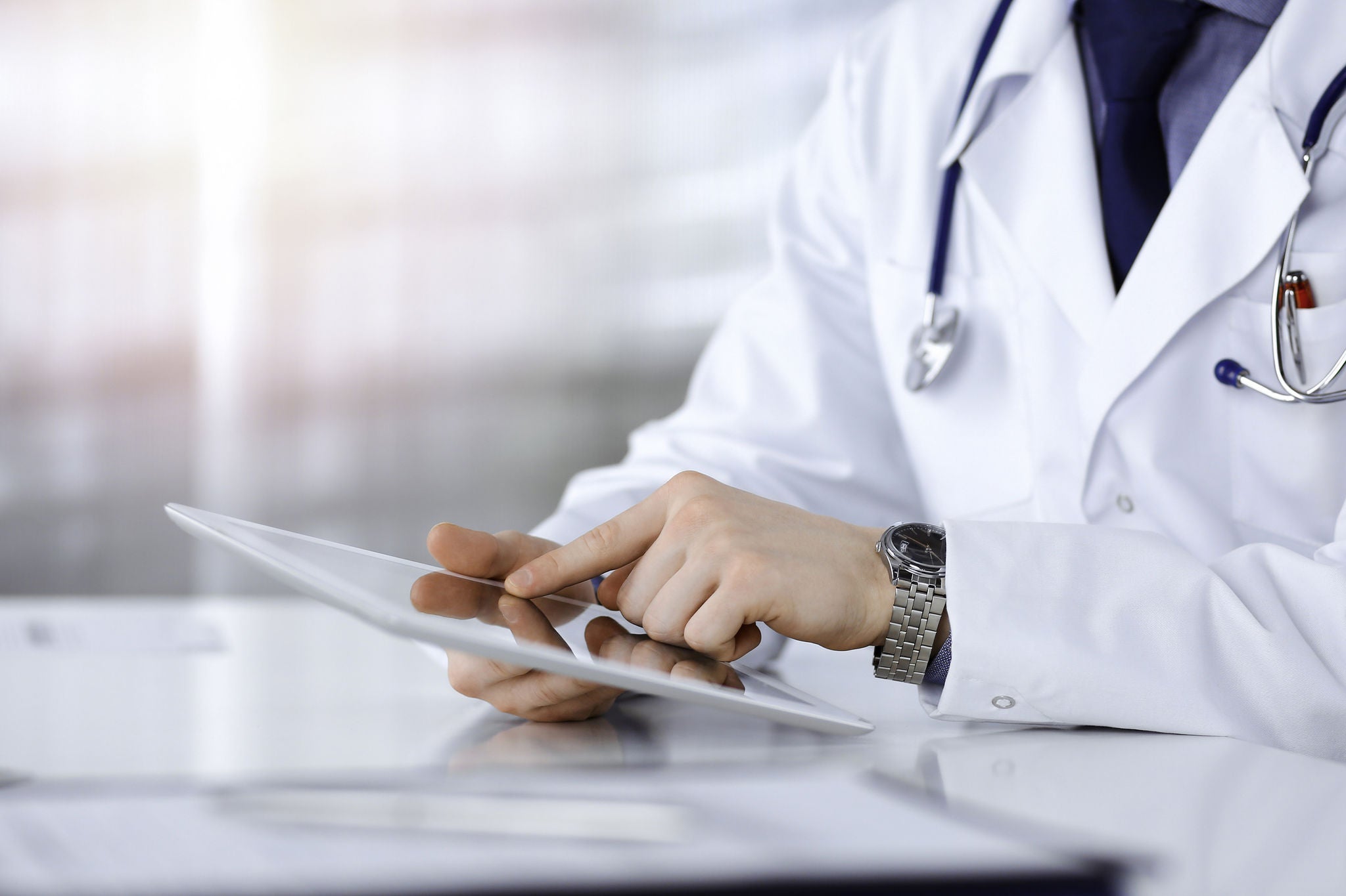 Unknown male doctor sitting and working with tablet computer iin a darkened clinic