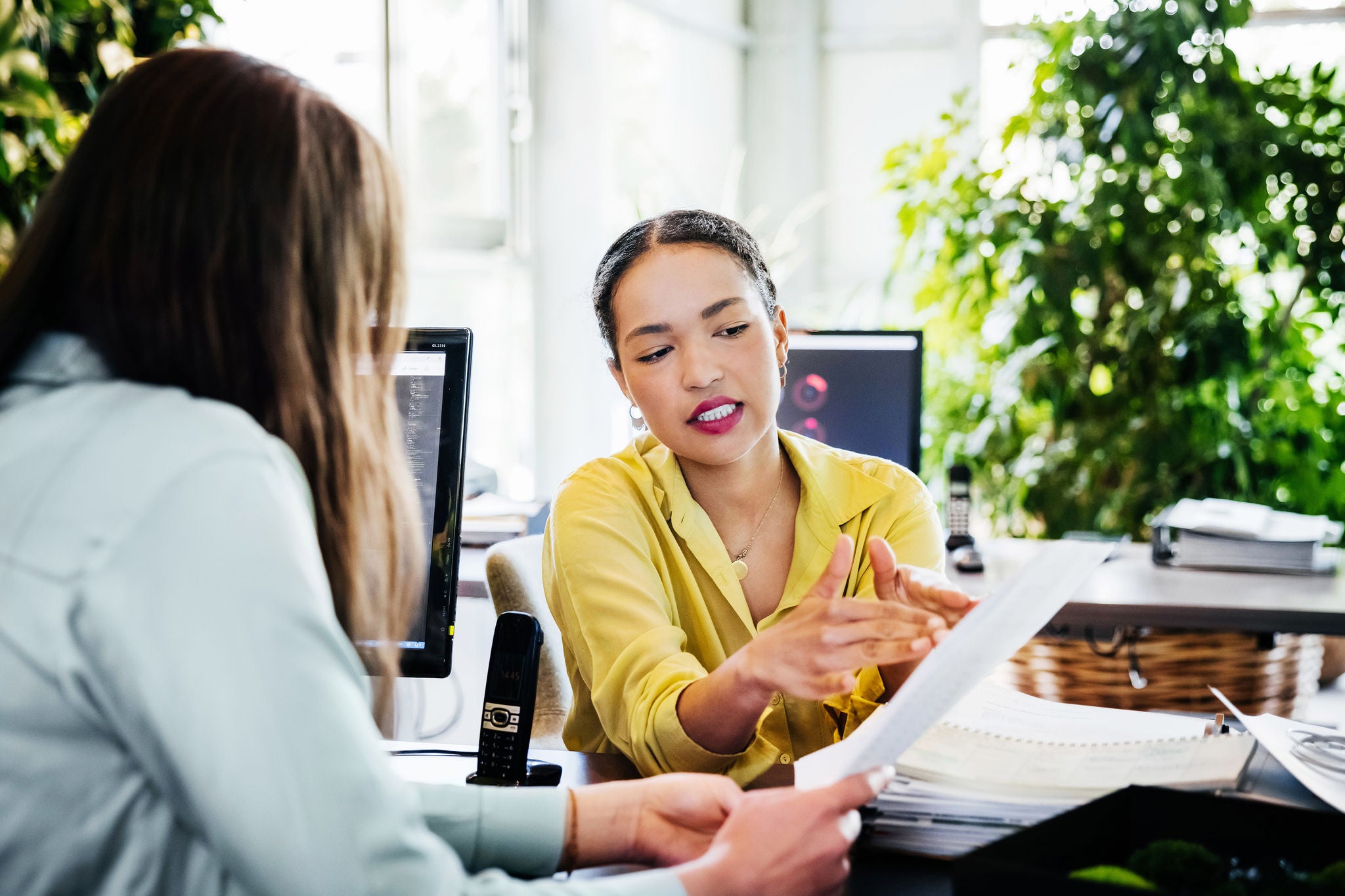 A woman looking at some paperwork with one of her colleagues in a modern and fresh office environment.